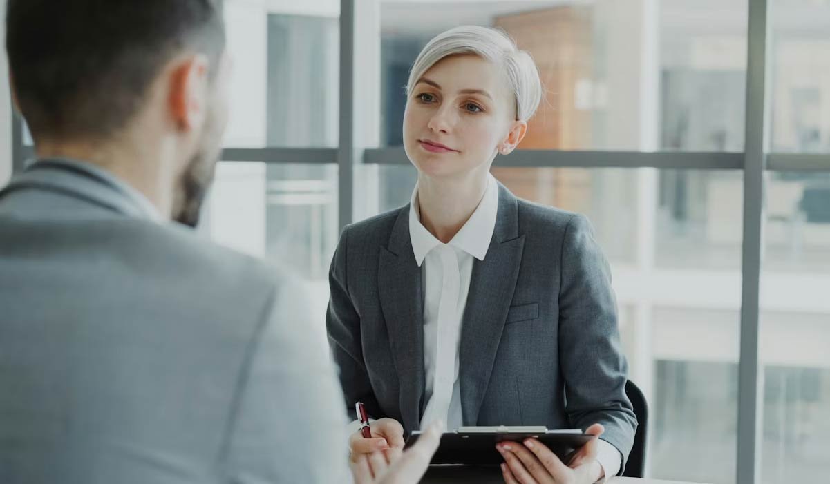 Woman in a grey suite interviewing a man. 
