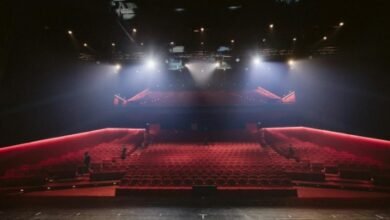 View from the stage of a large theatre auditorium with red seats and bright overhead lights, illustrating live performance venues associated with UK musical comedy